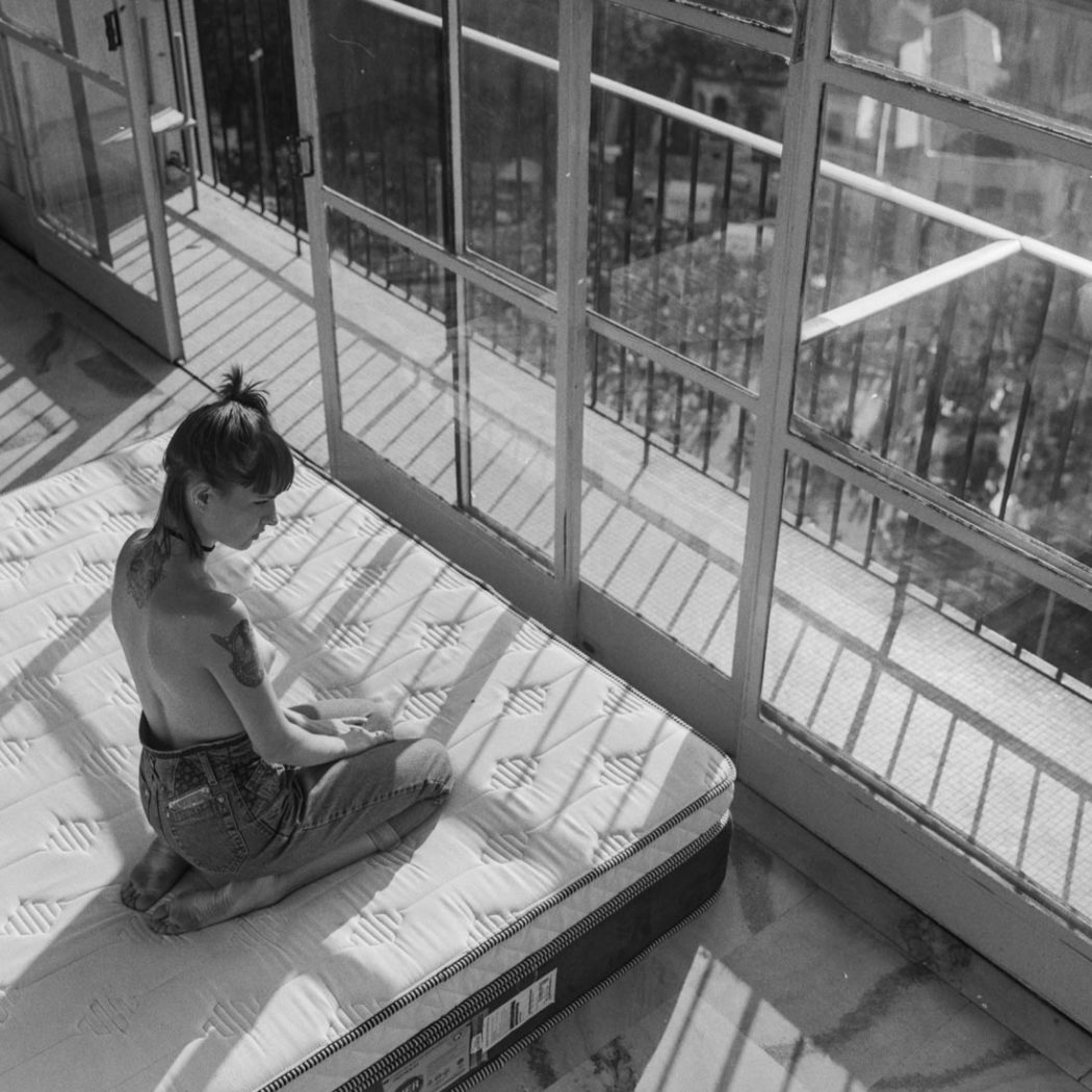 Modelo sentada em pose bucólica olhando para vista da cidade de São Paulo da varanda do apartamento