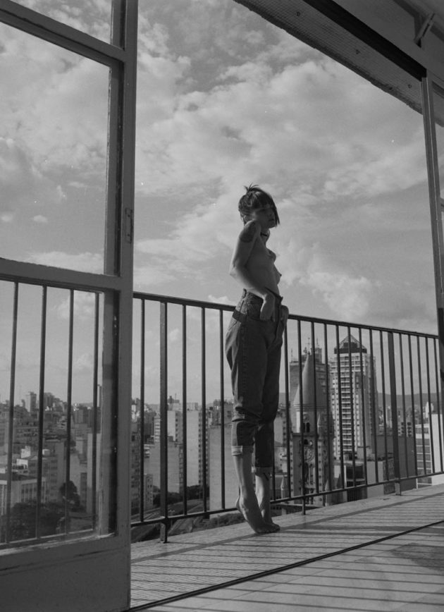 Modelo em pé na sacada do apartamento com vista para os prédios de São Paulo