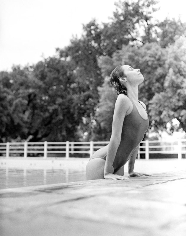 Modelo se esticando em borda de piscina com maiô body preto e branco