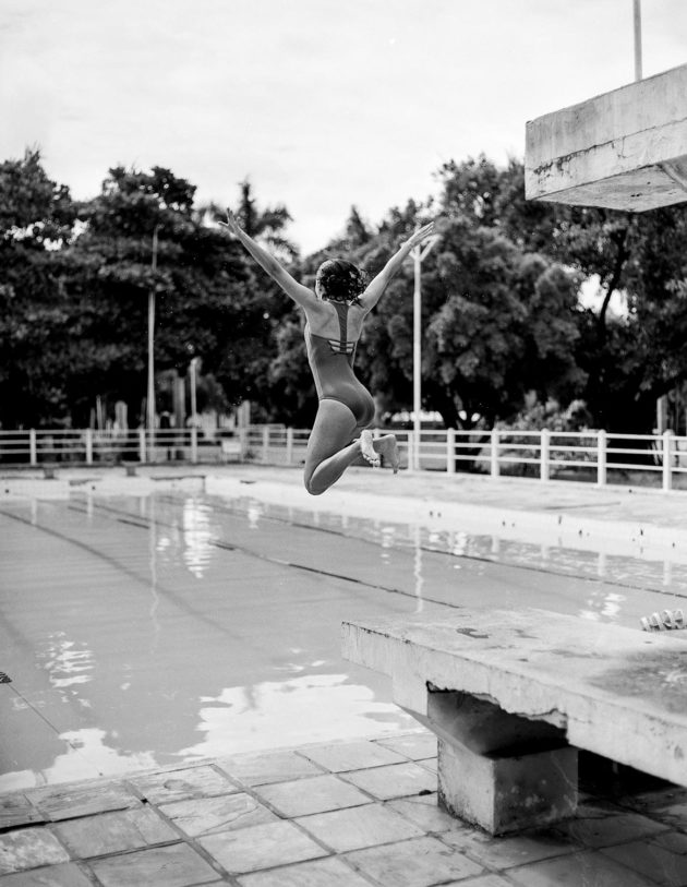 Modelo saltando em piscina com maiô body preto e branco