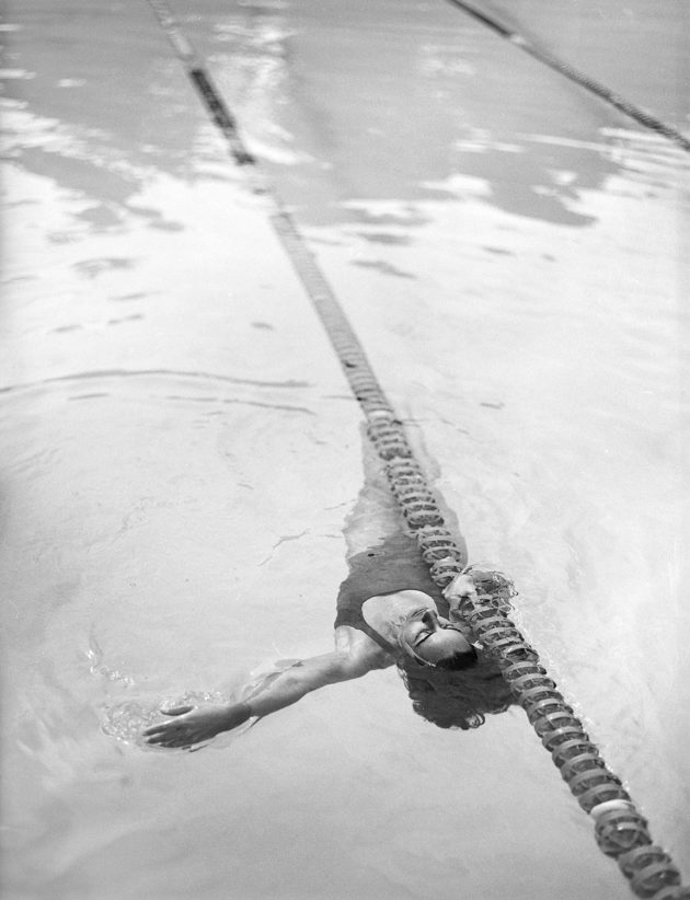 Modelo fotografada de cima em piscina olímpica nadando com body maiô