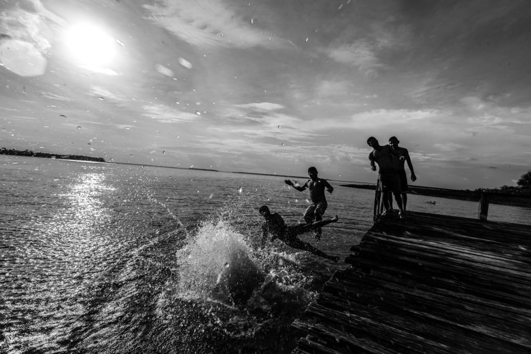 Garotos saltam juntos para o rio no Pará com luz do por do sol em preto e branco