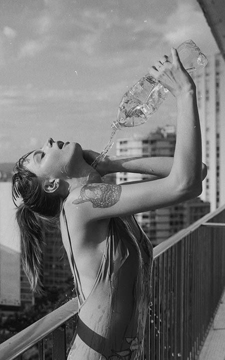 Modelo mulher jogando água em si mesma com garrafa da varanda do apartamento com vista para São Paulo