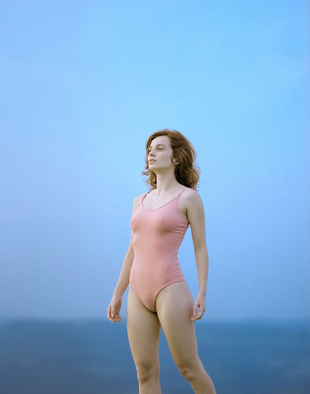 Retratos Feminino Bucólico em tons pastéis com fundo de céu azul e modelo de expressão distante e body rosa bebê claro