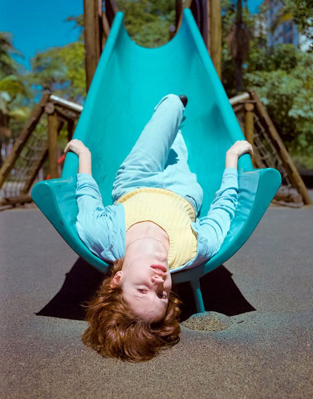 Modelo em pose exótica em playground com escorregador azul e roupas tons pastéis