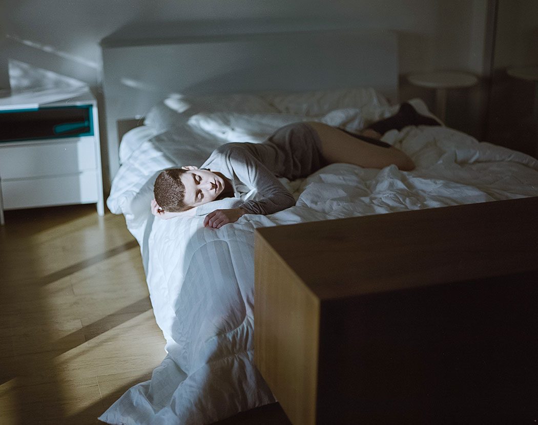 Modelo mulher deitada em cama sob luz de penumbra delicada e roupas cinza