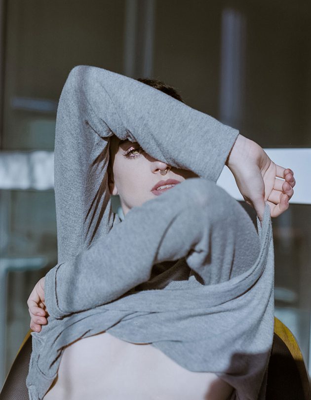 Modelo com tirando suéter cinza mostrando pele em pose sensual