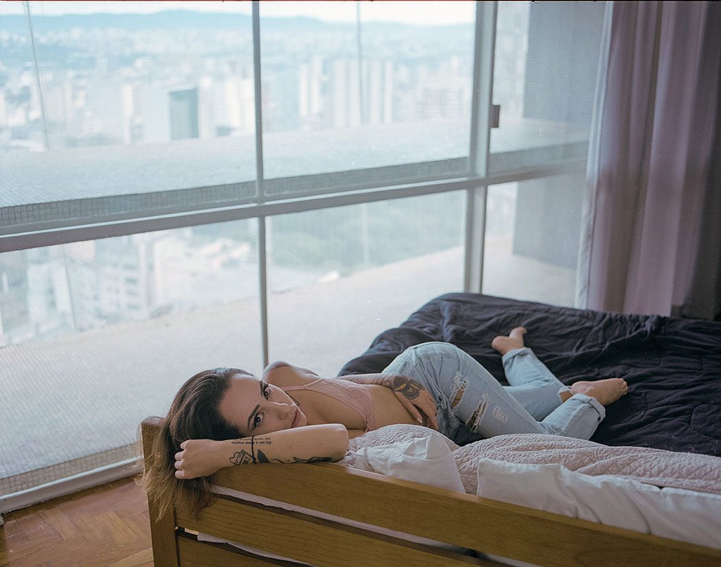 modelo deitada na cama em apartamento do edifício Copan com vista para a cidade em tons suaves