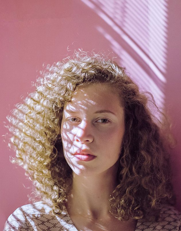 Retrato em close de modelo contra fundo rosa pastel com luz dura de persiana desenhando sombras