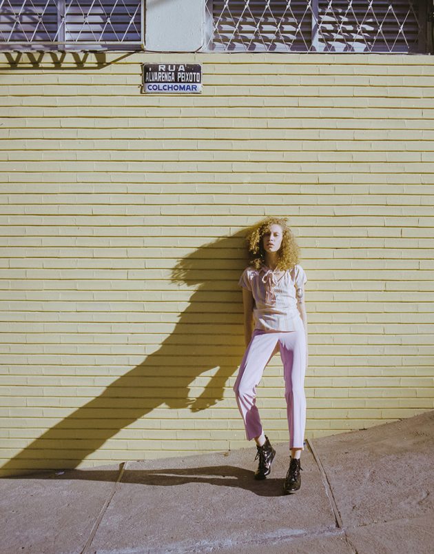 modelo em roupa rosa pastel contra parede amarela em luz dura do fim do dia