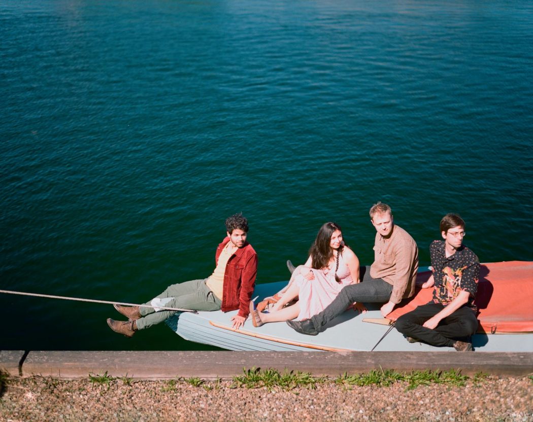 Banda musical de quatro integrantes sentados em cima de barco sobre água azul