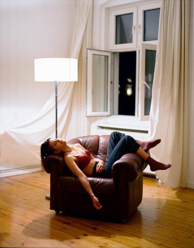 Garota de jeans deitada sobre sofá em apartamento moderno de luz quente
