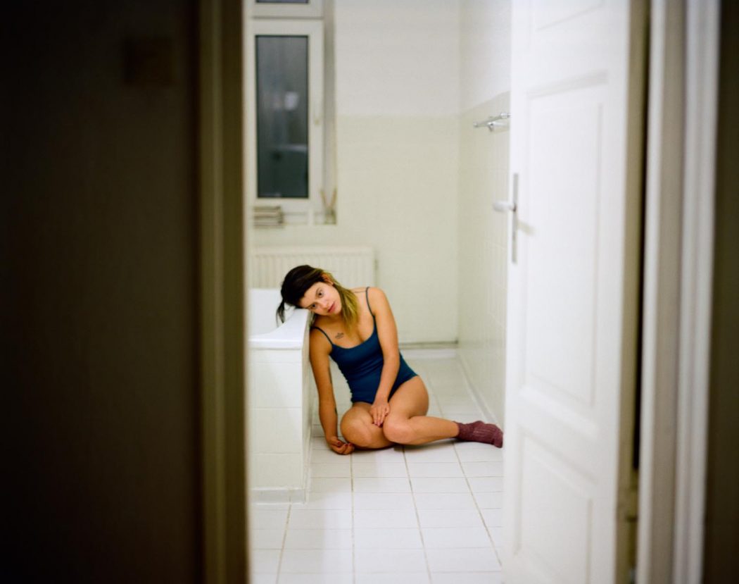 Garota de body maiô debruçada sobre banheira em banheiro branco retrô