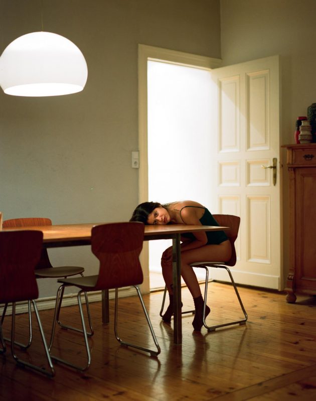 Garota debruçada sobre mesa sob iluminação quente interna de apartamento moderno