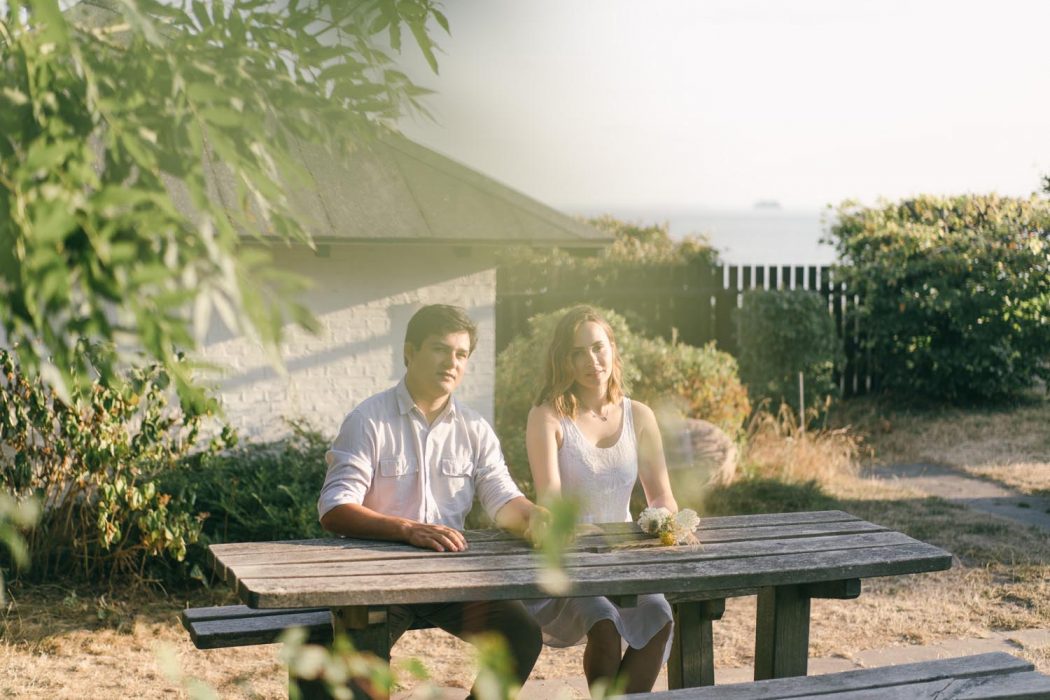 Casal sentado em mesa de madeira com natureza ao fundo durante ensaio de casal