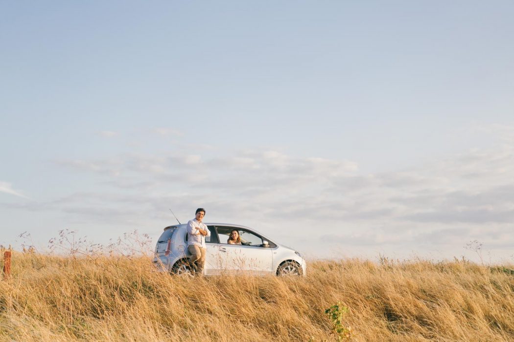 Casal no carro em campo de trigo amarelo com luz do pôr do sol durante ensaio de casal