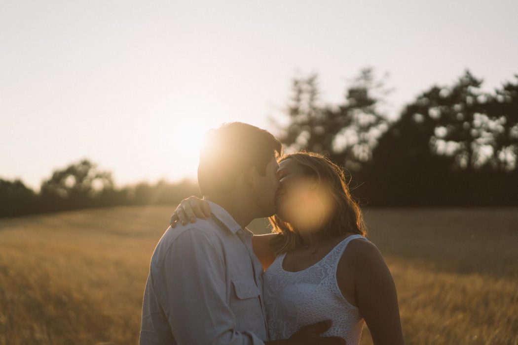 Casal se beijando em campo de trigo amarelo com luz do pôr do sol durante ensaio de casal