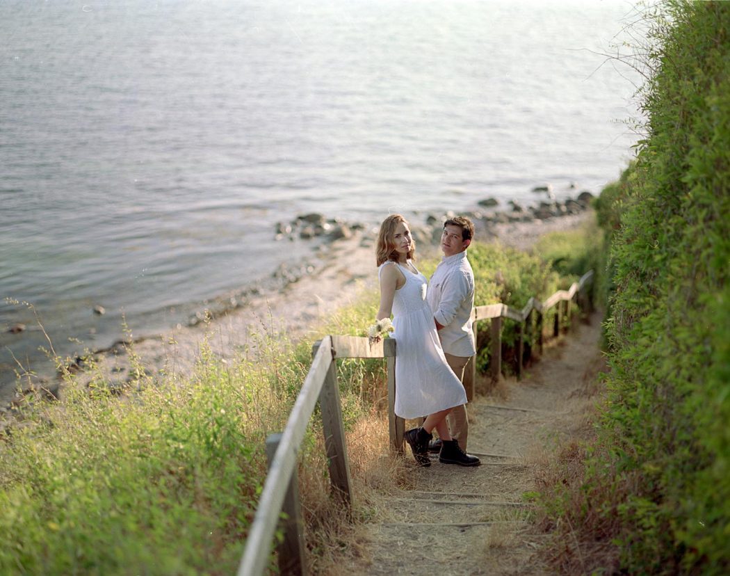 Casal em pé em escada de madeira na praia durante ensaio de casal