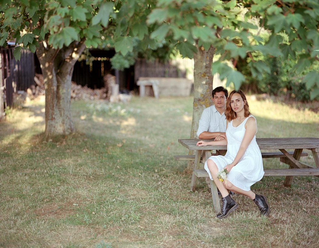 Casal sentado em mesa de madeira com natureza ao fundo durante ensaio de casal