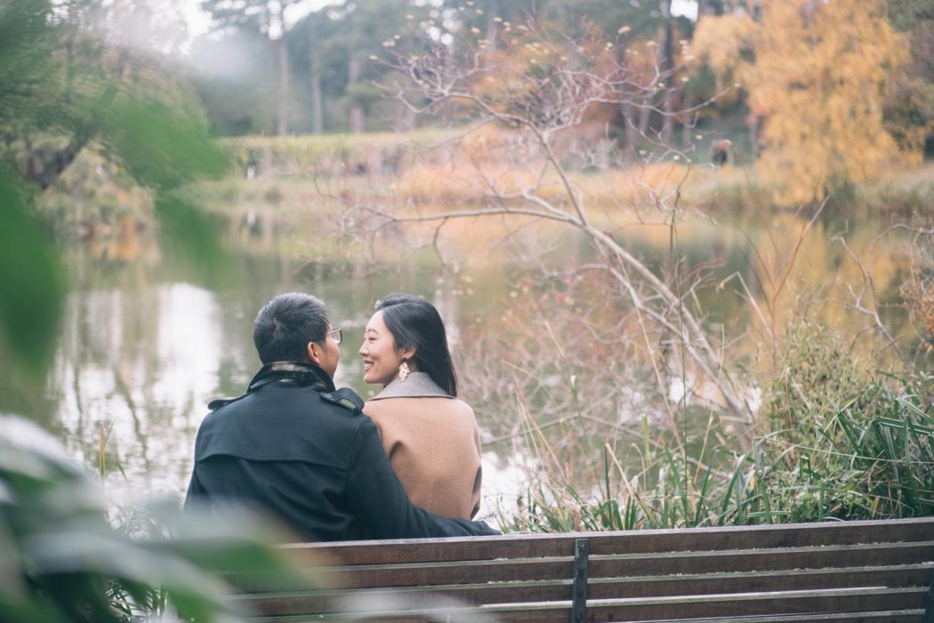 Casal sentado em banco de frente para o lago com vista para paisagem de natureza