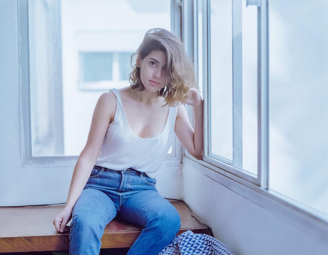 Garota branca do cabelo curto sentada próximo à janela de calça jeans