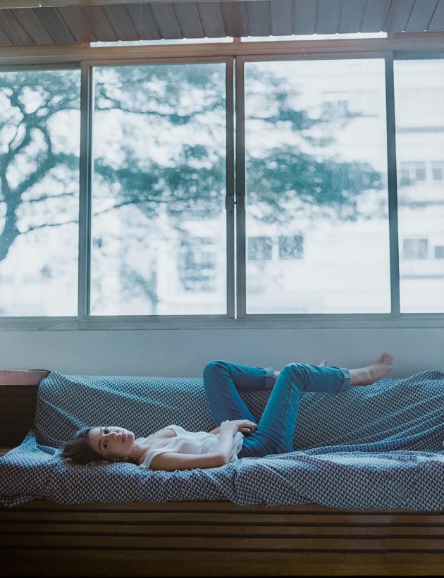 Garota branca do cabelo curto deitada próximo à janela de calça jeans