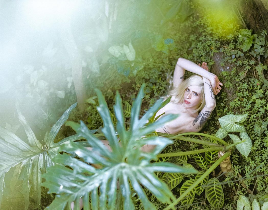 Garota menina loira branca de olhos azuis claros com natureza verde ao fundo deitada