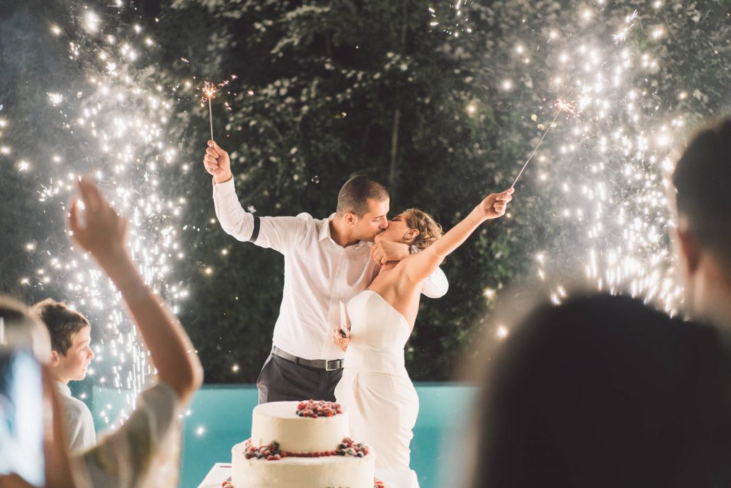 Noiva e noivo beijando com fogos de artifício em recepção de casamento