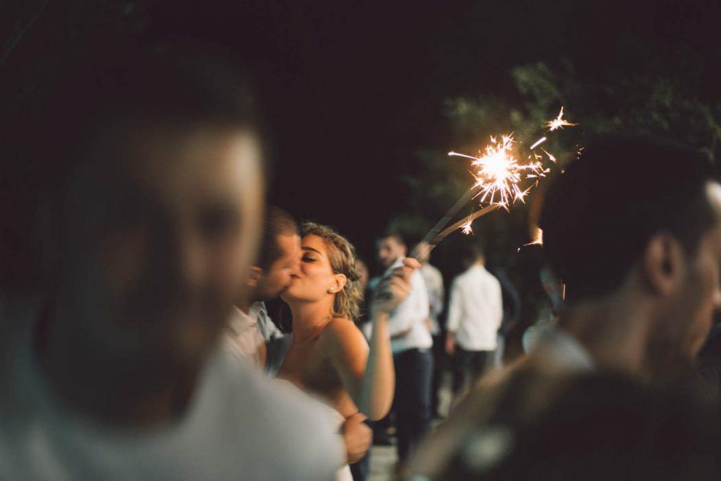 Noiva e noivo beijando com fogos de artifício em recepção de casamento