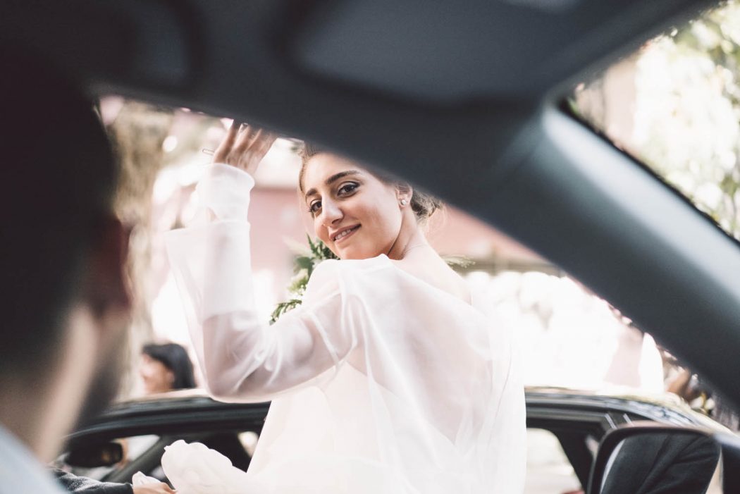 Noiva de branco dando tchau acenando para noivo dentro do carro