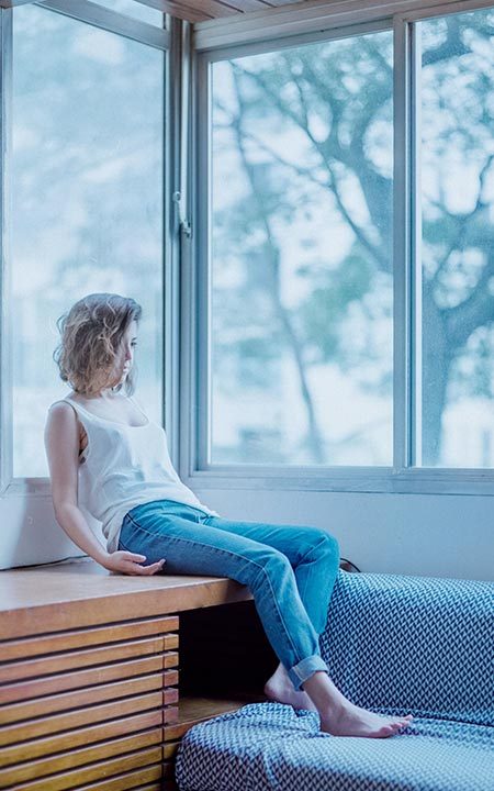 Garota branca do cabelo curto sentada próximo à janela de calça jeans