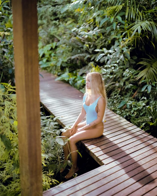 Garota menina loira sentada em deck de madeira em meio à naturza com luz do sol