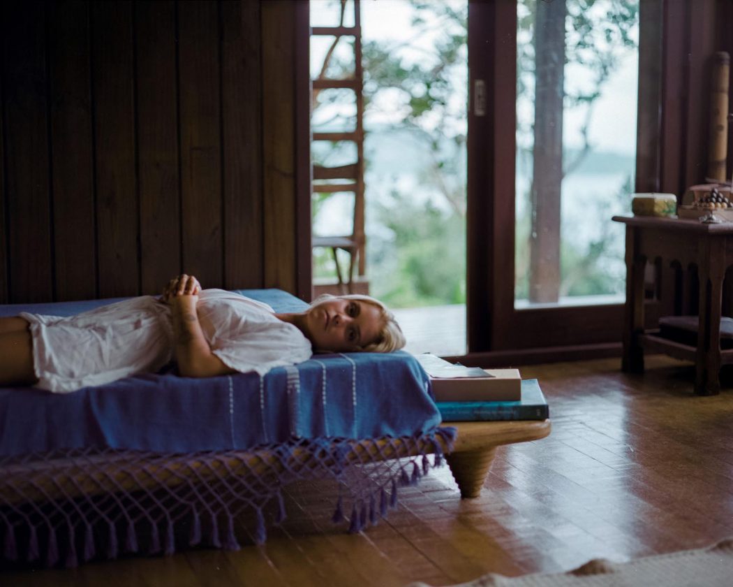 Garota menina loira deitada em casa de madeira com natureza ao fundo