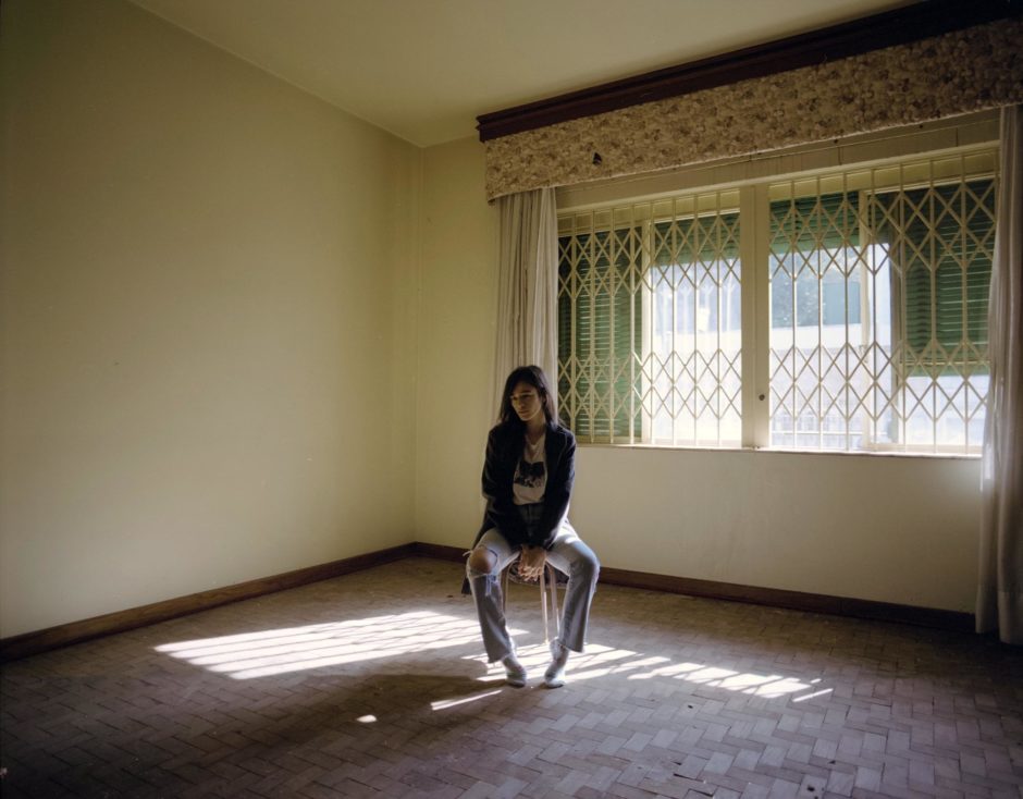 Garota sentada em sala vazia com luz entrando pela janela